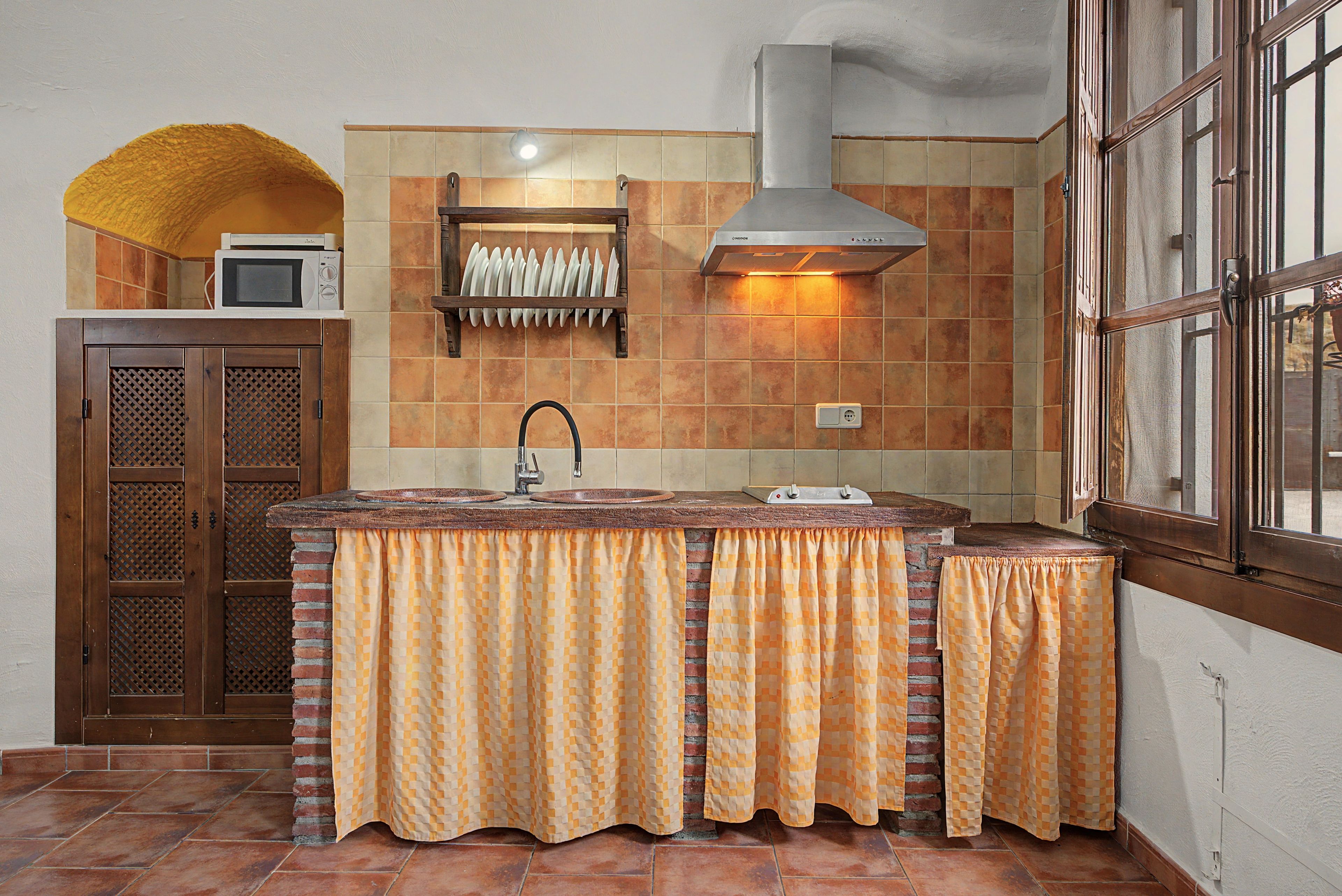 Une cuisine avec un mur recouvert de carreaux, un four à micro-ondes, une cuisinière et une fenêtre avec des barreaux.