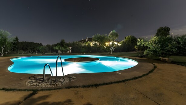 A swimming pool with a stone surround, surrounded by a lawn and trees. - Country House 'Los Jazmines' with Shared Pool, Wi-Fi and Air Conditioning (Benalúa)