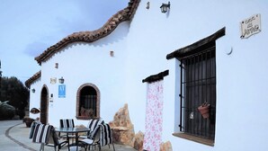 A white building with a tiled roof, a stone wall, and a patio with a table and chairs. - Country House 'Los Jazmines' with Shared Pool, Wi-Fi and Air Conditioning (Benalúa)
