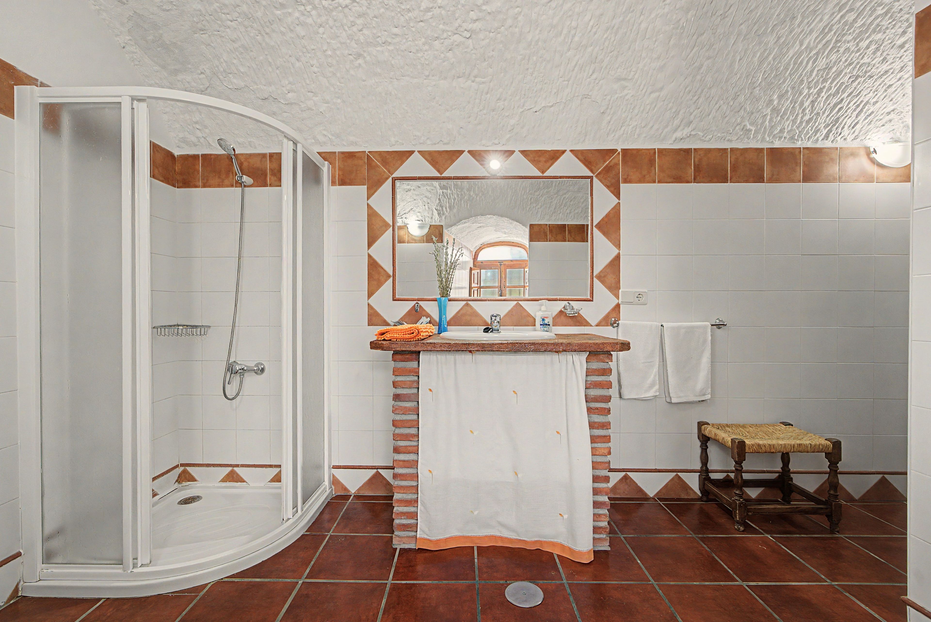 Une salle de bain avec une douche, un lavabo avec un miroir et un petit tabouret en bois.