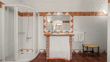 Une salle de bain avec une douche, un lavabo avec un miroir et un petit tabouret en bois.