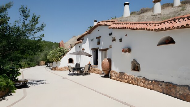 Un edificio blanco con tejas de arcilla, paredes de piedra y un patio con mobiliario exterior.