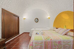 Une chambre avec une armoire en bois, un lit recouvert d’une courtepointe aux couleurs vives, un miroir au mur et un mur d’accent jaune.