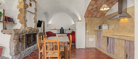 A rustic kitchen with stone walls, a tiled floor, and a dining area with wooden furniture.