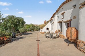 Une cour avec une table et des chaises, un tonneau et un bâtiment blanc doté d’un toit en tuiles.