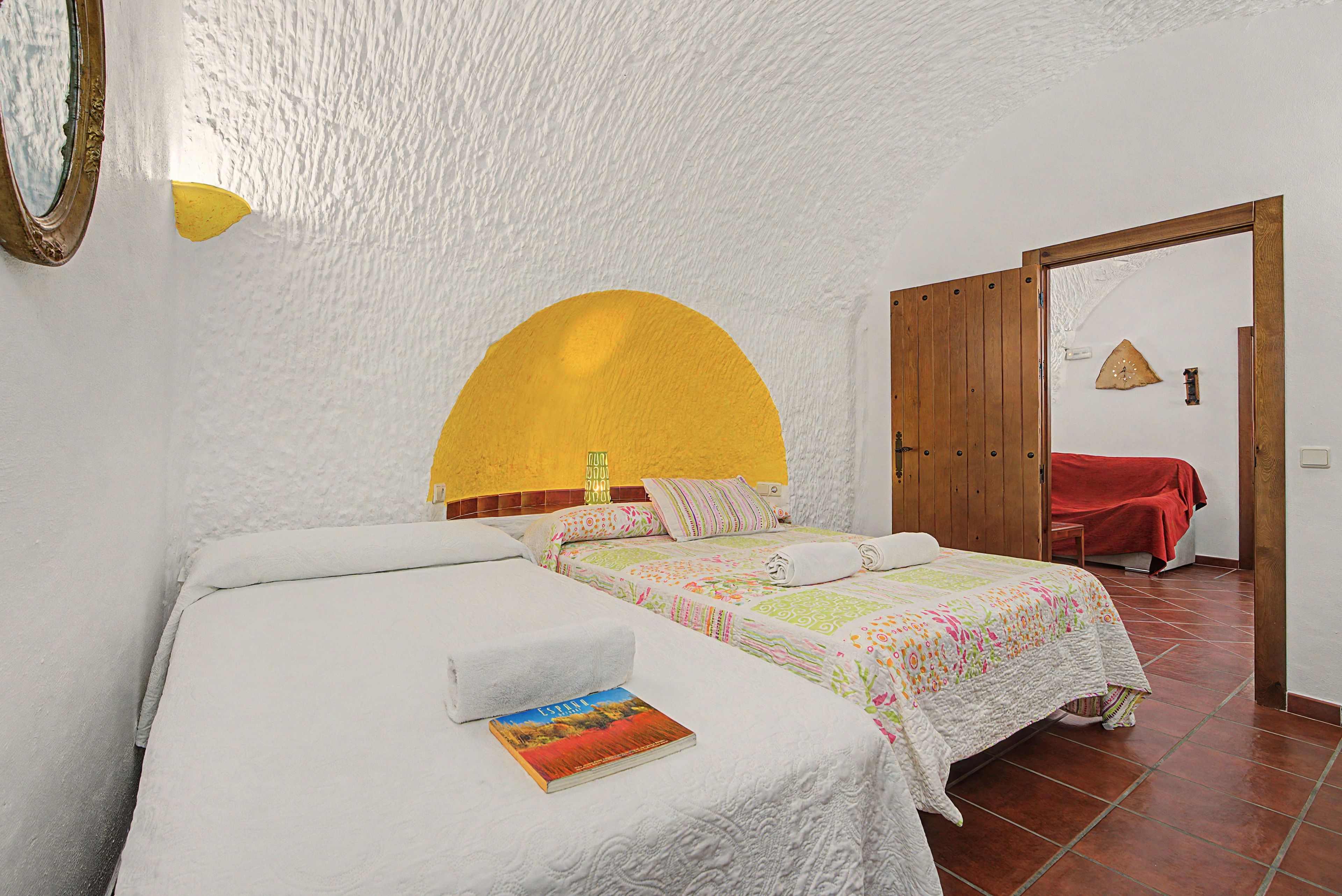 A bedroom with a single bed, a bedside table, a book, and a wooden door leading to another room.