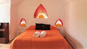 Una habitación con una cama, dos lámparas adosadas a la pared y un techo abovedado singular.