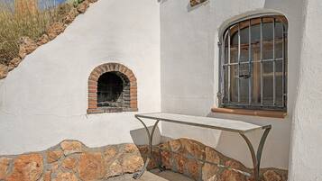 Un edificio blanco con base de piedra, una pequeña ventana en arco y una mesa de metal al frente.