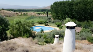 Una piscina rodeada de hierba seca y árboles, con una estructura blanca al frente.