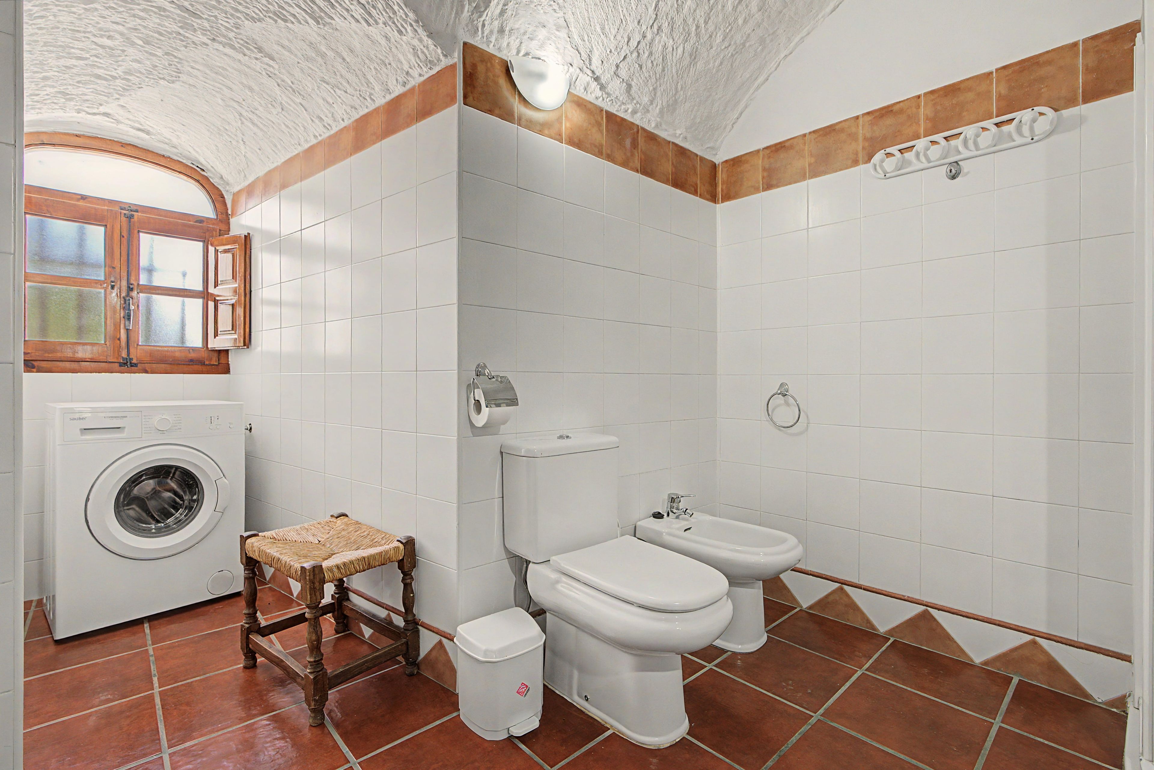 Une salle de bain équipée d’un lave-linge, d’un petit tabouret en bois, de toilettes et d’un bidet.