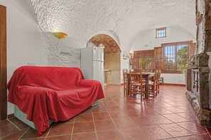 Un salon chaleureux avec un canapé rouge, une table à manger avec des chaises et un coin cuisine doté de meubles en bois et d’une fenêtre.