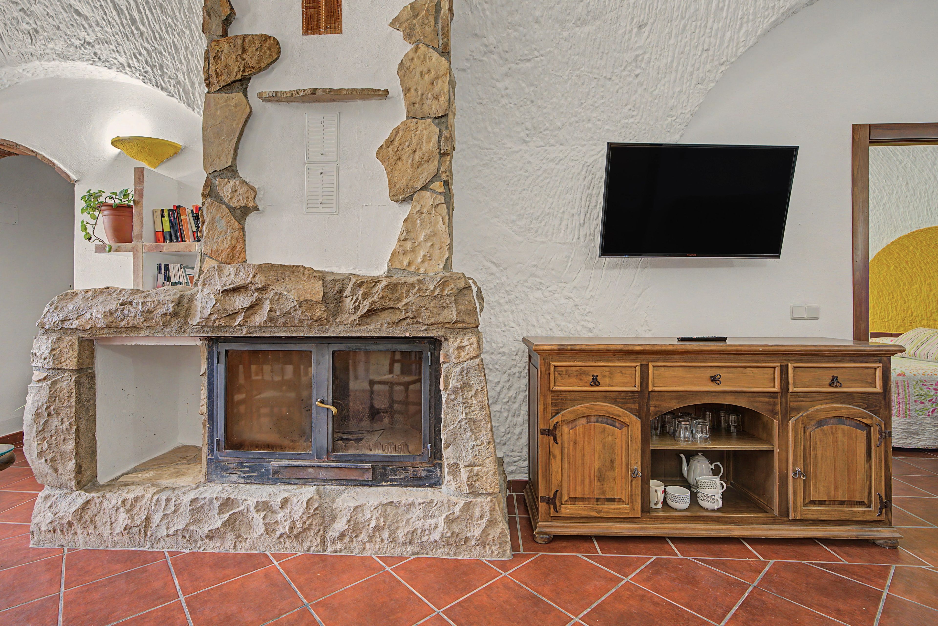Una chimenea de piedra con un televisor encima, un mueble de madera con utensilios de cocina y un piso de baldosas.