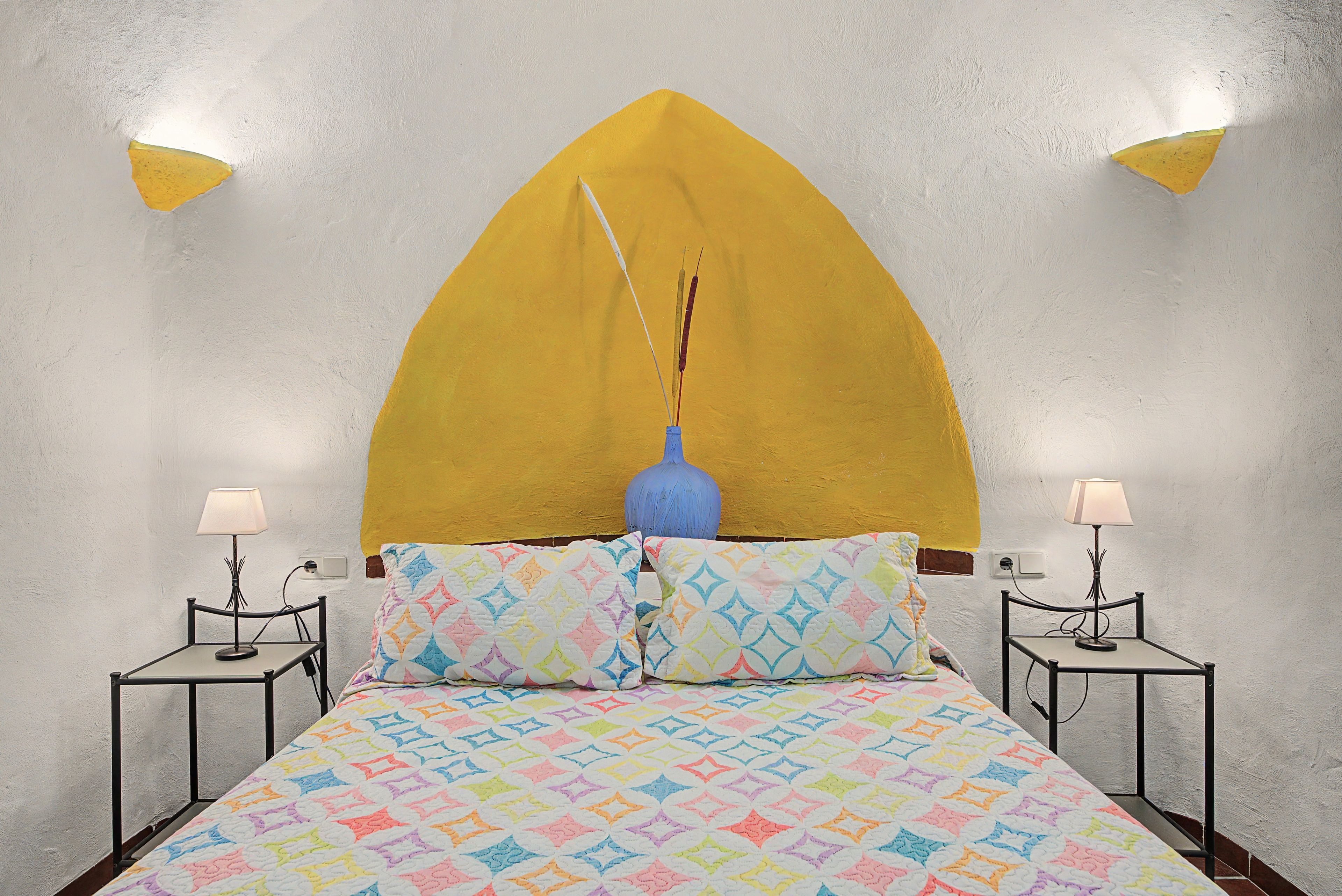 A bed with a geometric patterned bedspread, a blue vase on the headboard, and two bedside lamps on either side.