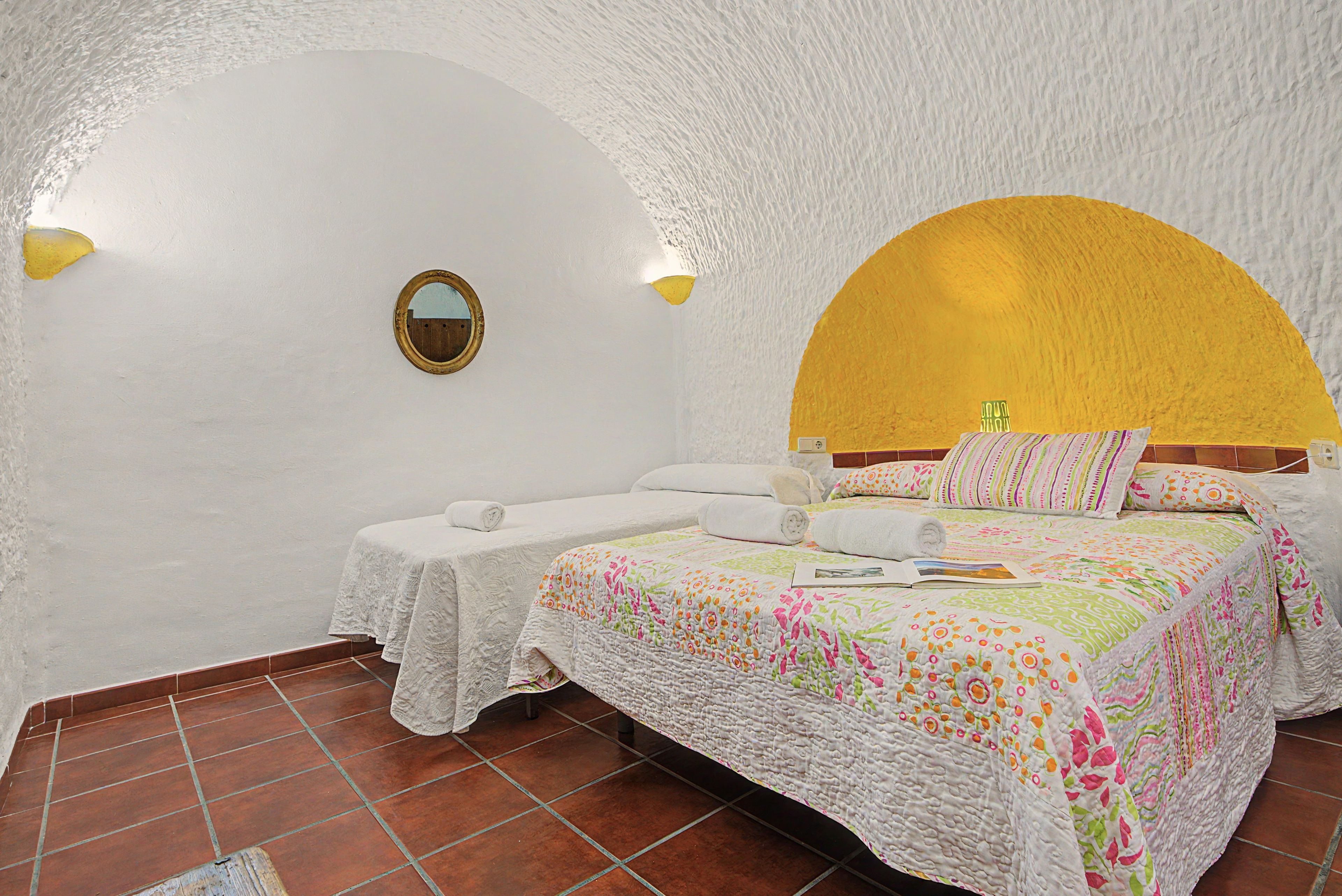 Ein Zimmer mit einem Bett, einer Bank, einem Spiegel und einem gelben Bogen über dem Bett.