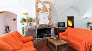 Una sala de estar acogedora con chimenea de piedra, dos sofás naranja y un televisor.