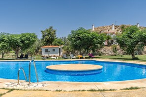 Una piscina con zona circular de hidromasaje, rodeada de sillones de descanso y un pequeño edificio.