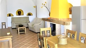 Ein gemütliches Wohnzimmer mit Sofa, Sesseln, einem Esstisch und einer Küchenzeile mit Kühlschrank.