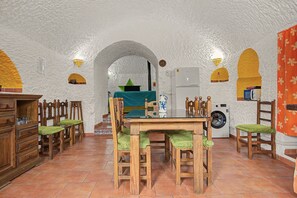 A compact kitchen with a dining area, featuring a washing machine, wooden furniture, and a tiled floor.