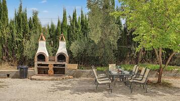 An outdoor seating area with two brick ovens, a table with chairs, and a tree.
