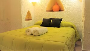 Ein Zimmer mit einem Bett, Kissen, einem zusammengerollten Handtuch, einer Vase und einer Wandleuchte.