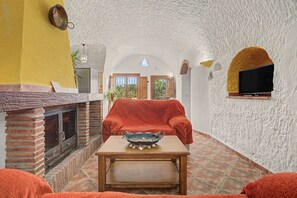 Un intérieur chaleureux avec une cheminée en briques, un canapé rouge et un téléviseur fixé à un mur à texture.