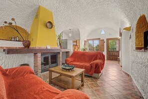 A rustic interior with a brick fireplace, a yellow wall, and a cozy seating area with orange cushions. - Country House 'El Olivo' with Shared Pool, Wi-Fi and Air Conditioning (Benalúa)