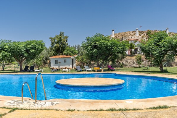 Une piscine avec un espace de jacuzzi circulaire, entouré de chaises longues et d’un petit bâtiment.