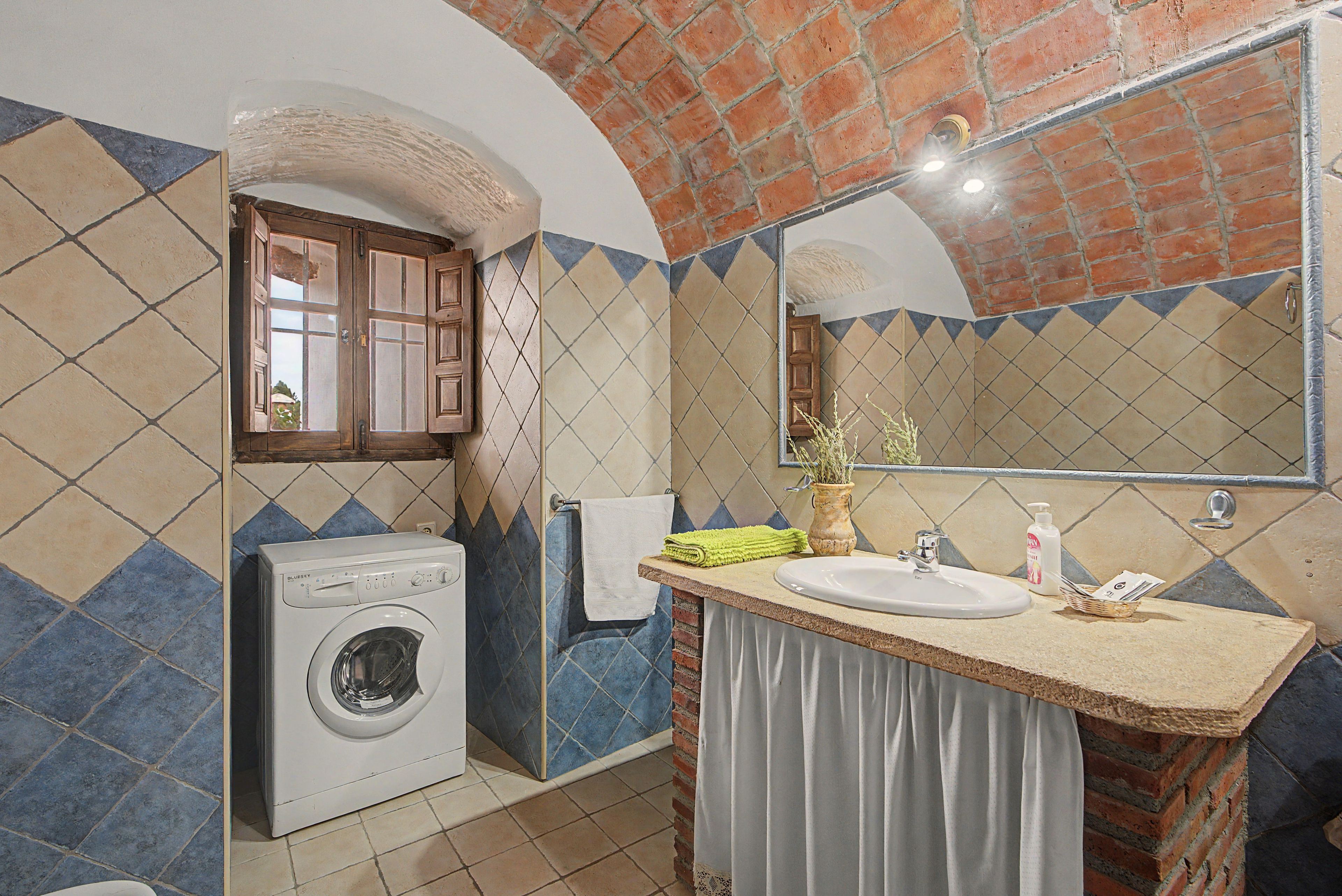 Une petite salle de bain équipée d’un lave-linge, d’un lavabo et d’un miroir.