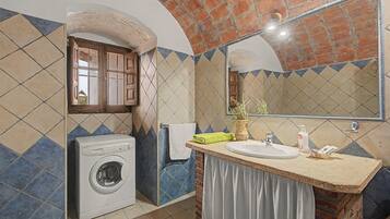 Une petite salle de bain équipée d’un lave-linge, d’un lavabo et d’un miroir.