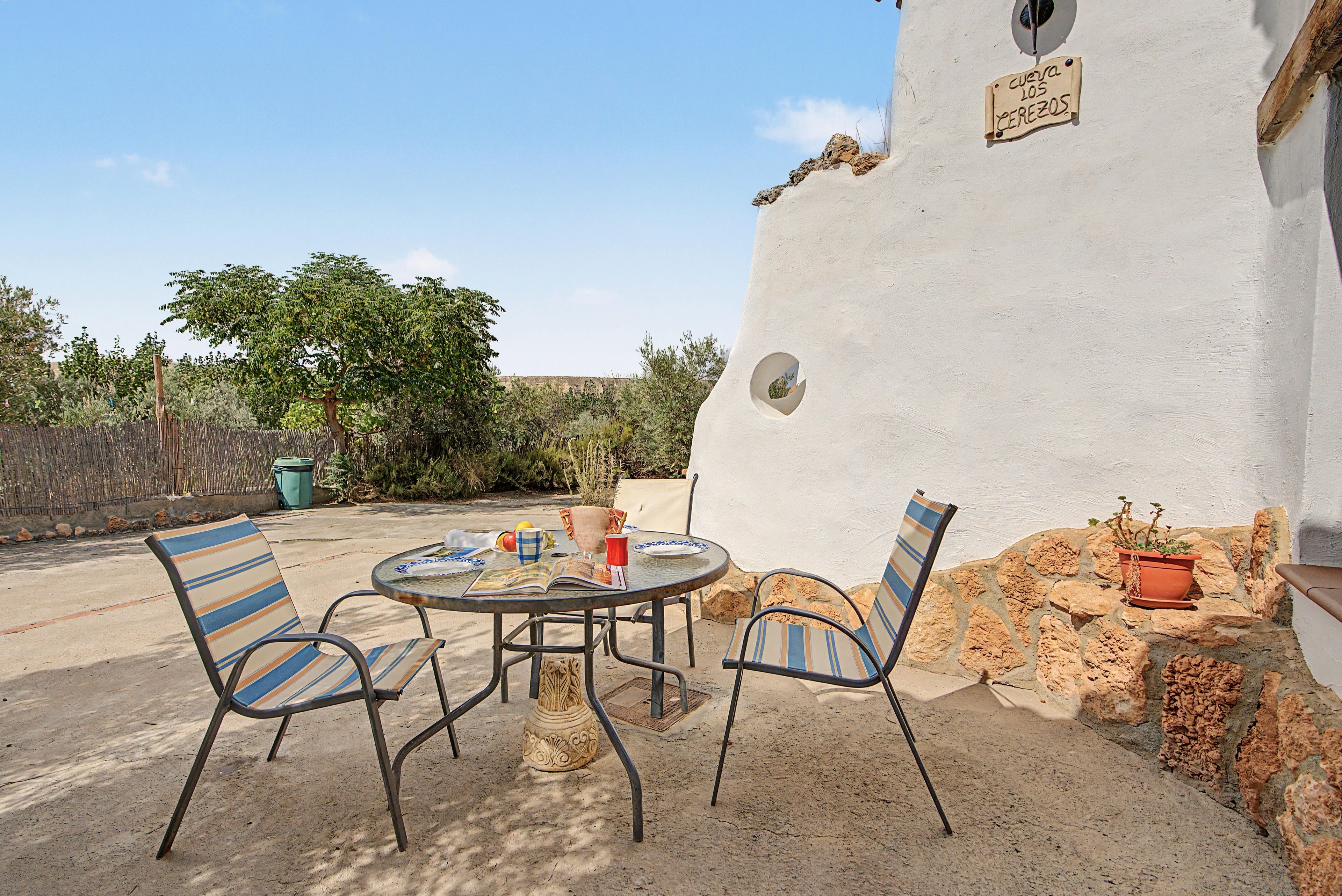 Un patio exterior con una mesa redonda y sillas a rayas, una planta en maceta y una pared con un letrero.