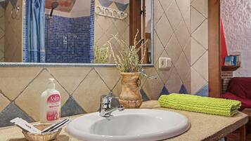 Een badkamer met een witte wastafel, een spiegel, een douchegordijn en een vaas met gedroogde planten.
