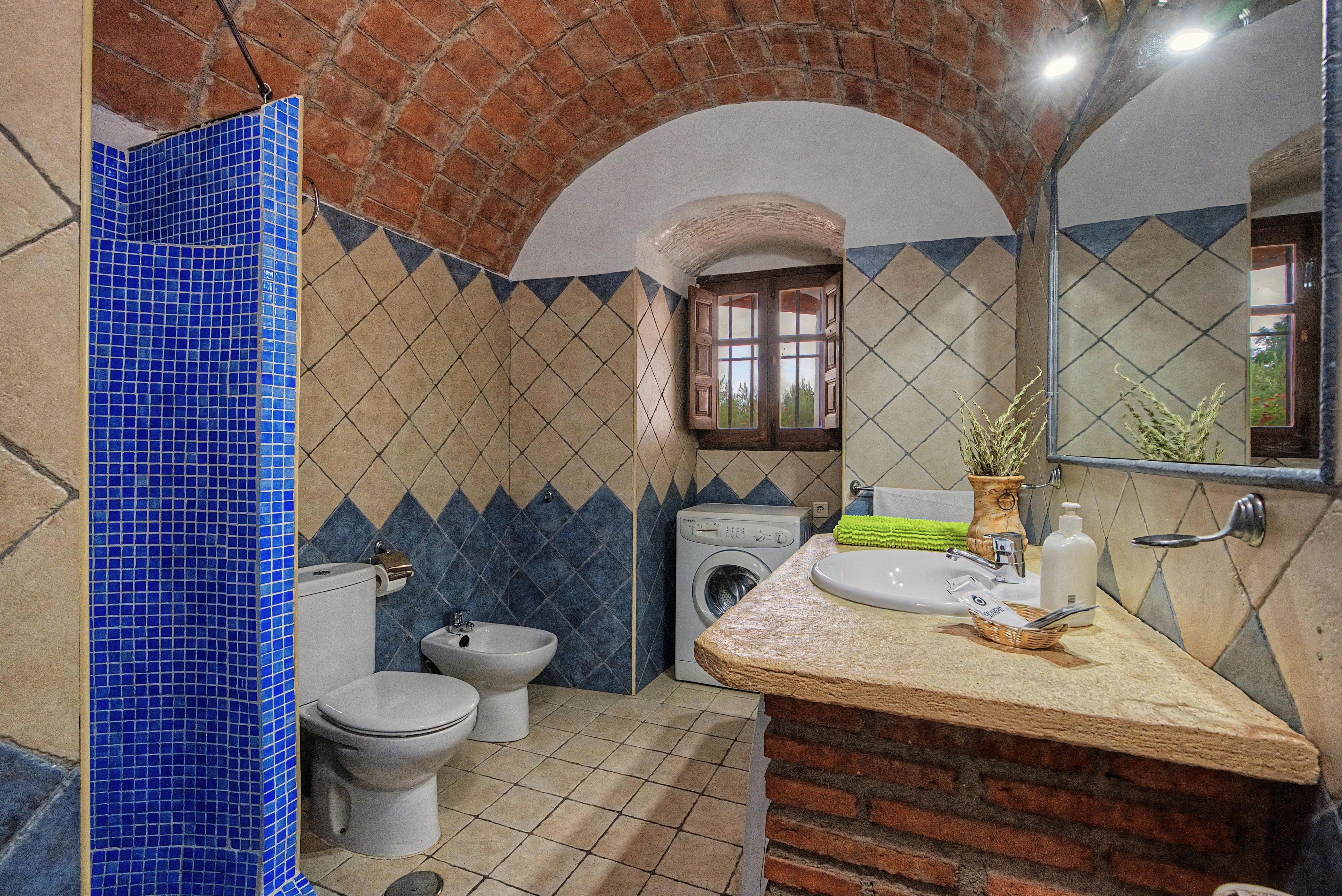 Un baño con pared de azulejos, lavadora, inodoro y lavamanos con espejo.