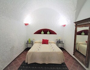 Ein Schlafzimmer mit einem Bett, zwei Nachttischen, einem Spiegel und einem roten Bogen über dem Bett.