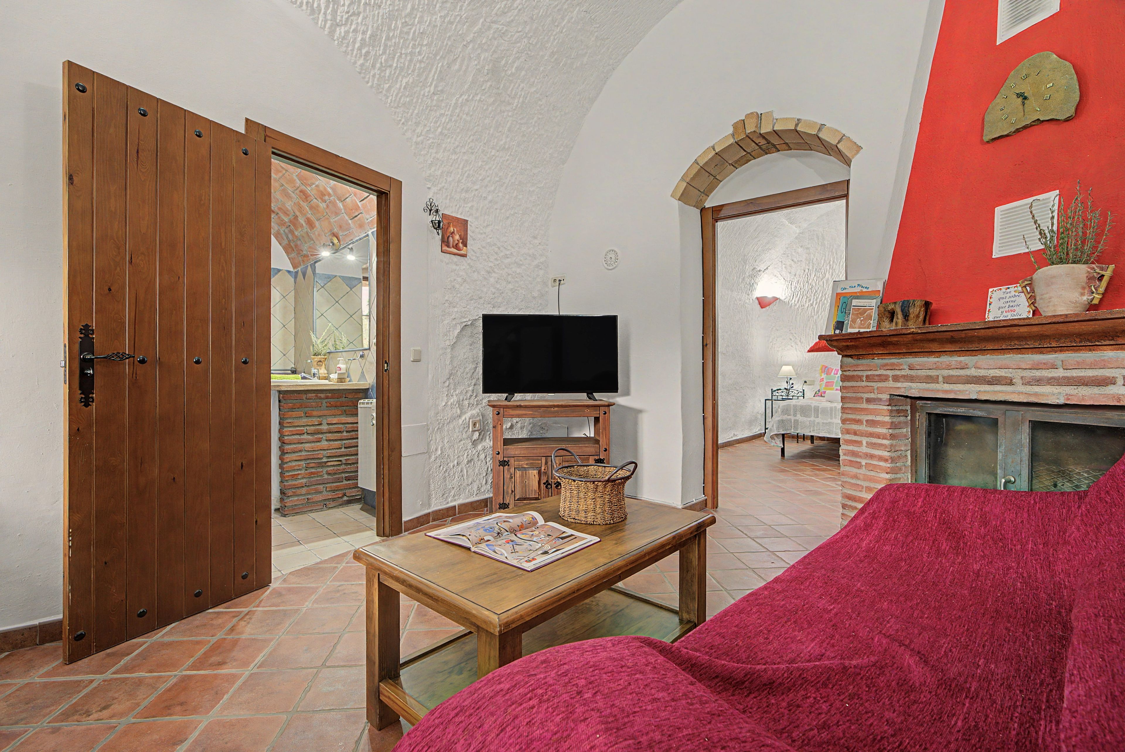 Een woonkamer met een televisie, een open haard, een rode stoel en een houten tafel.