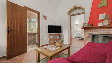 Een woonkamer met een televisie, een open haard, een rode stoel en een houten tafel.
