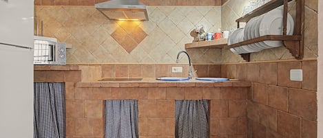 A kitchen with a built-in oven, a sink, and a shelf with dishes.