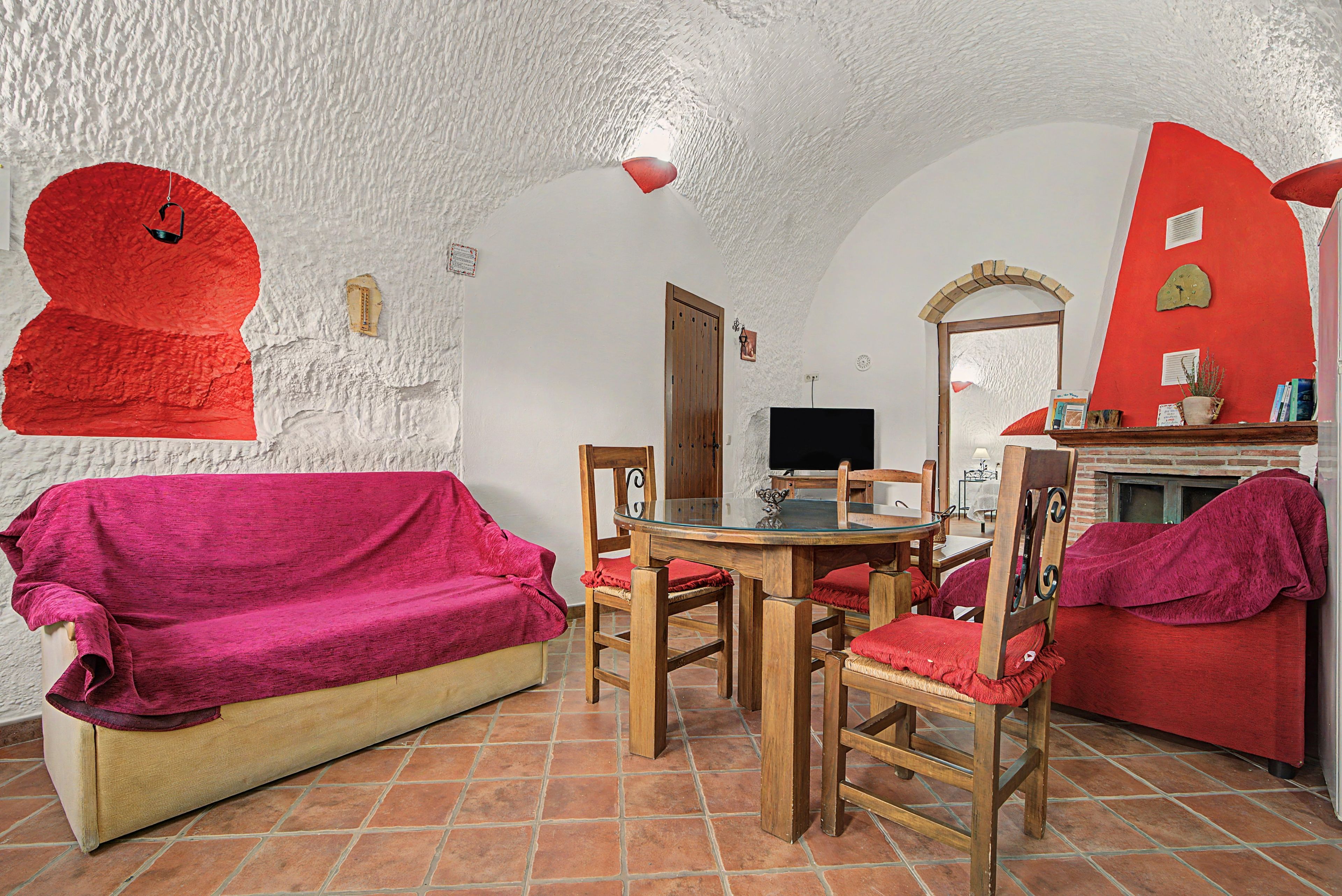 Una habitación acogedora con un sofá rojo, una mesa de comedor de madera con sillas, un televisor y una chimenea.
