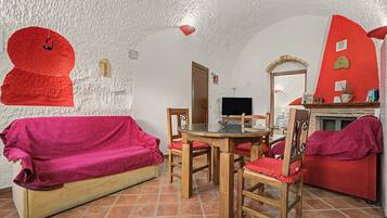 Una habitación acogedora con un sofá rojo, una mesa de comedor de madera con sillas, un televisor y una chimenea.