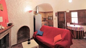 Ein gemütliches Wohnzimmer mit Kamin, einem roten Sofa und einer Küche im Hintergrund.