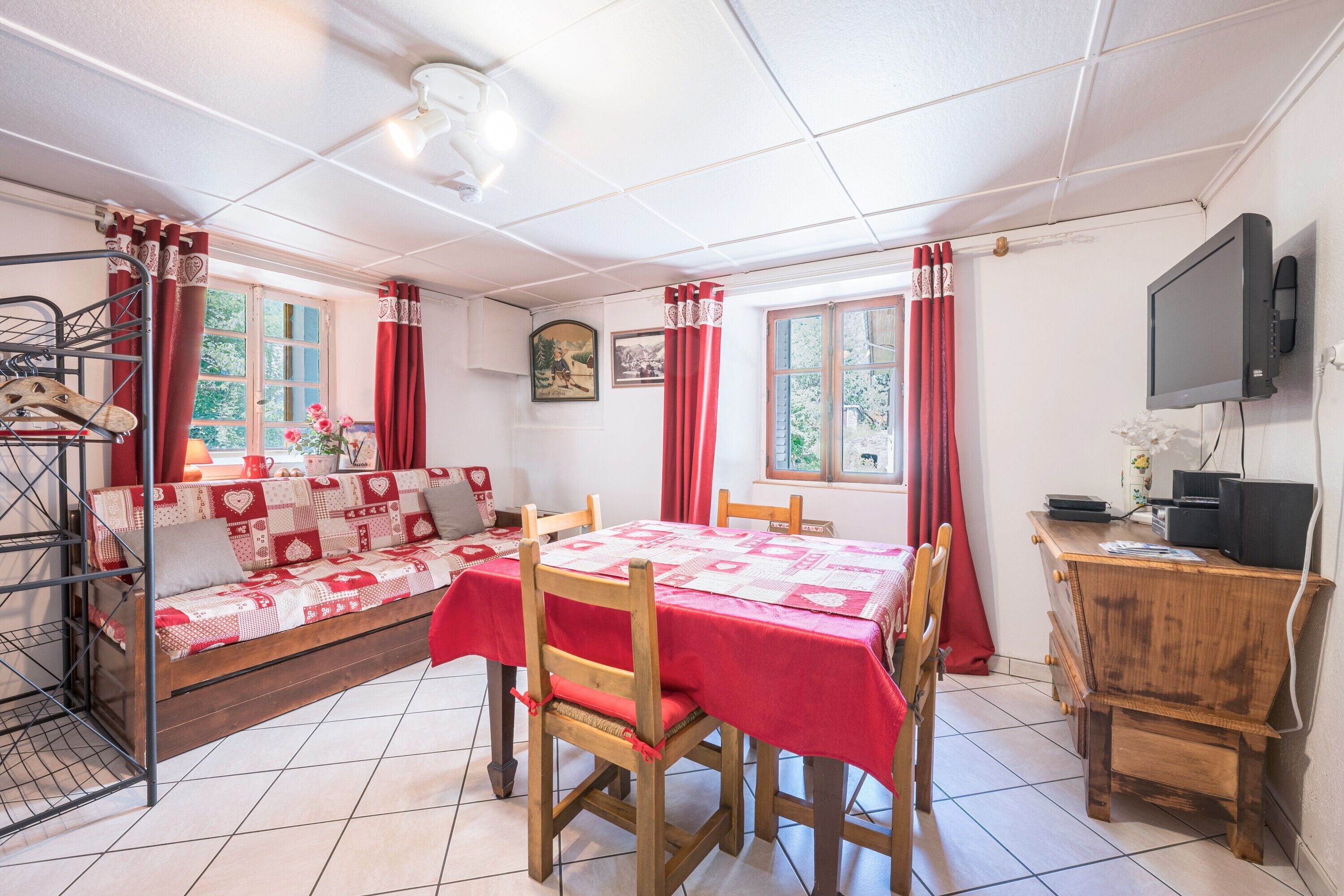 A room with a bed, a dining table, chairs, a TV, and a window with curtains.