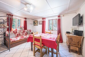 Una habitación con cama, una mesa de comedor, sillas, un televisor y un ventanal con cortinas.