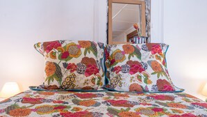 A bed with floral-patterned bedding and pillows, a mirror, and a wall with a stone texture. - Apartment 'Rose Des Neiges' with Mountain View, Shared Garden and Wi-Fi (Valloire)