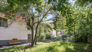 A courtyard with a bench, trees, and buildings in the background. - Apartment 'Rose Des Neiges' with Mountain View, Shared Garden and Wi-Fi (Valloire)
