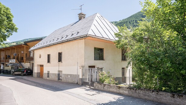 A small building with a sloped roof, a gated entrance, and a paved street in front. - Apartment 'Rose Des Neiges' with Mountain View, Shared Garden and Wi-Fi (Valloire)