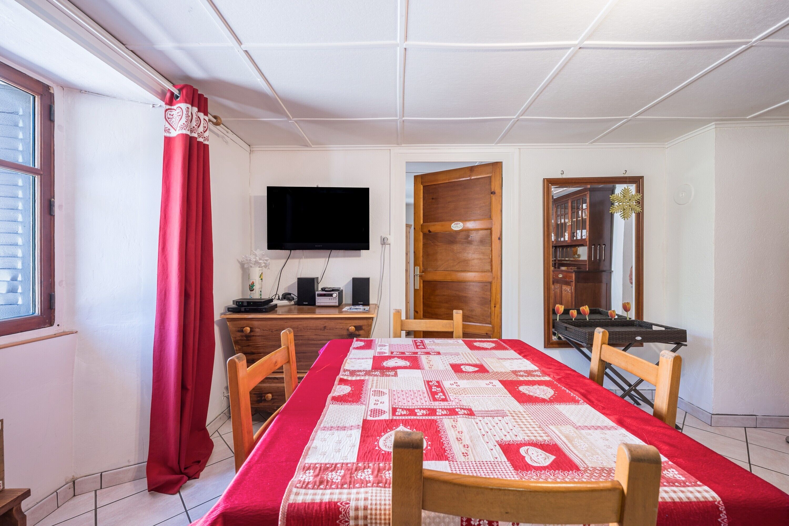 A dining area with a long table, chairs, a TV, and a wooden door.