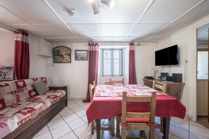 Un comedor con una mesa lista para cuatro personas, un sofá, un televisor y una ventana con cortinas.