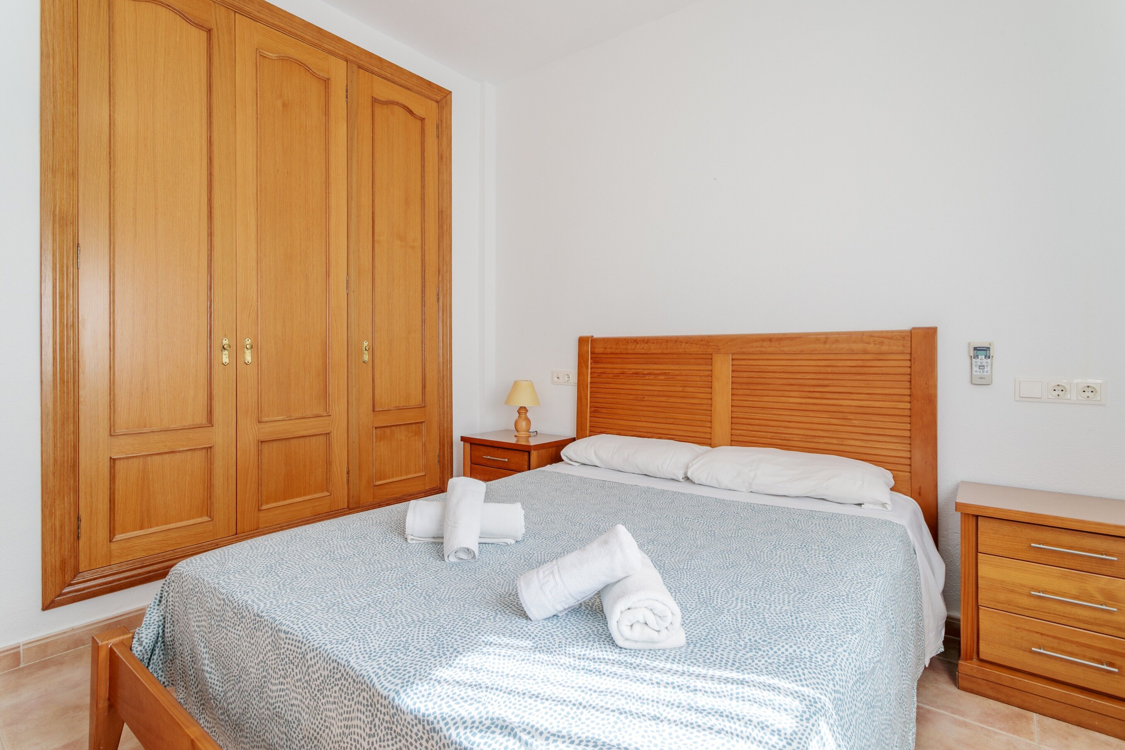 Un dormitorio con un armario de madera grande, una cama con colcha estampada y toallas dobladas con cuidado.