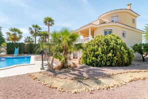 Una casa de dos pisos con piscina, palmeras y un jardín bien cuidado.