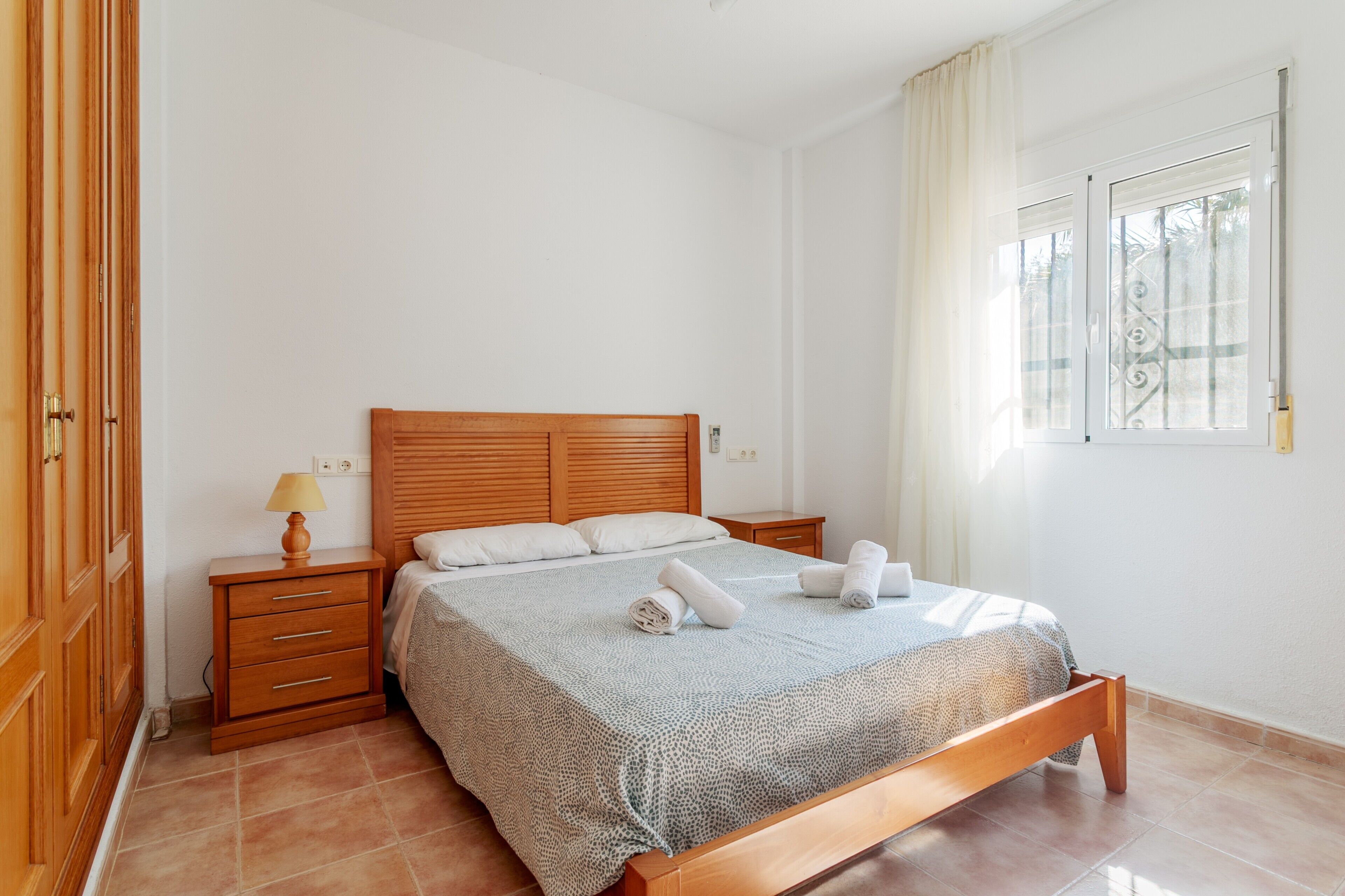 Une chambre à coucher avec un lit en bois, une table de chevet, une lampe et une fenêtre avec des rideaux.