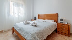 A neatly made bed with a wooden headboard, a bedside table with a lamp, and a nightstand with a clock. - Holiday Home 'Limonita' with Private Pool, Wi-Fi and Air Conditioning (Mutxamel)